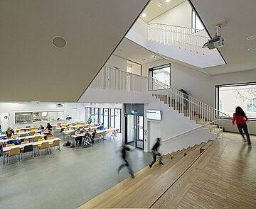 Blick von der Holztreppe auf den Speisesaal und den Eingangsbereich der Ganztageseichrichtung.