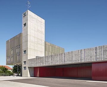 Blick auf einen Teil der gräulichen Nordfassade, die im Kontrast zu den roten Schiebtüren der Fahrzeughalle steht.