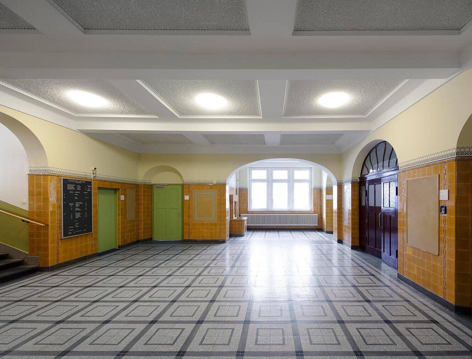 Blick in ein Foyer mit historischen Wandfliesen, Türen und saniertem Steinboden.