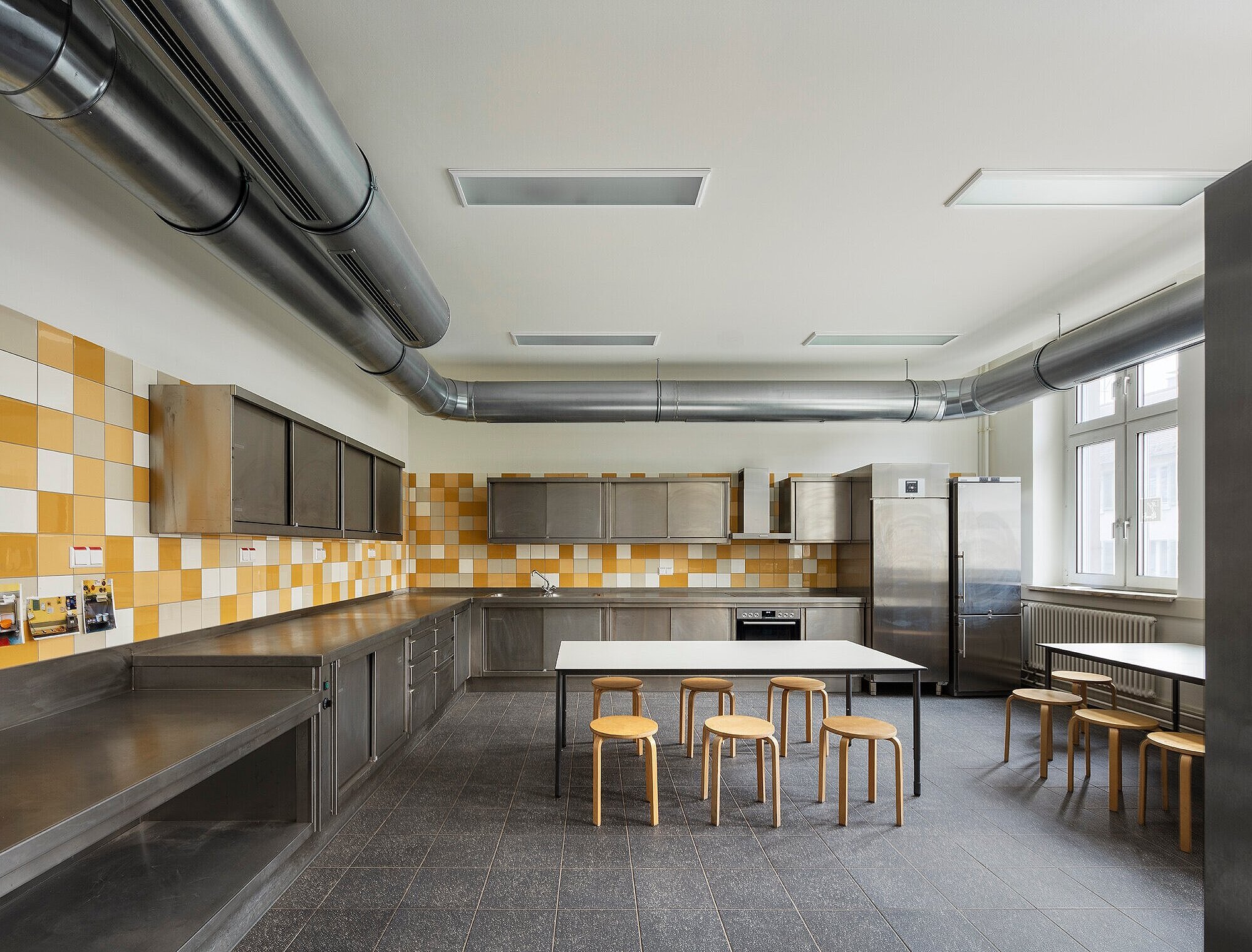 Blick in einen Küchenraum mit zwei Arbeitstischen und Stühlen in der Mitte.