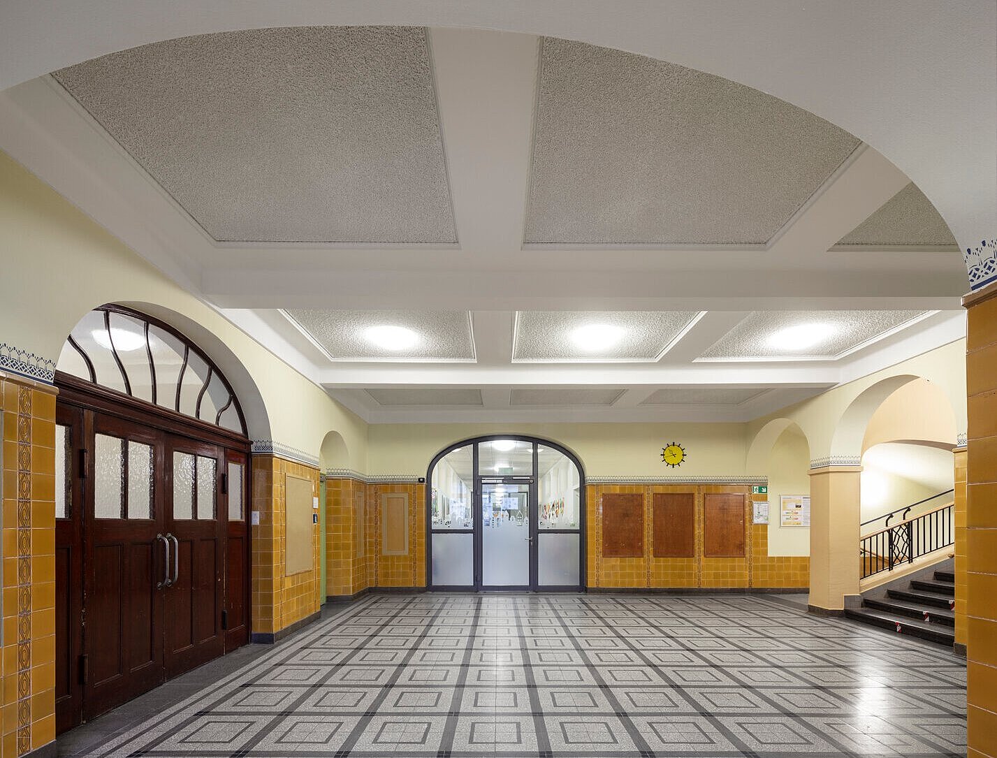 Blick in ein Foyer mit historischen Wandfliesen, Türen und saniertem Steinboden.