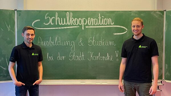 Zwei Personen stehen vor einer Schultafel auf der Schulkooperation steht.