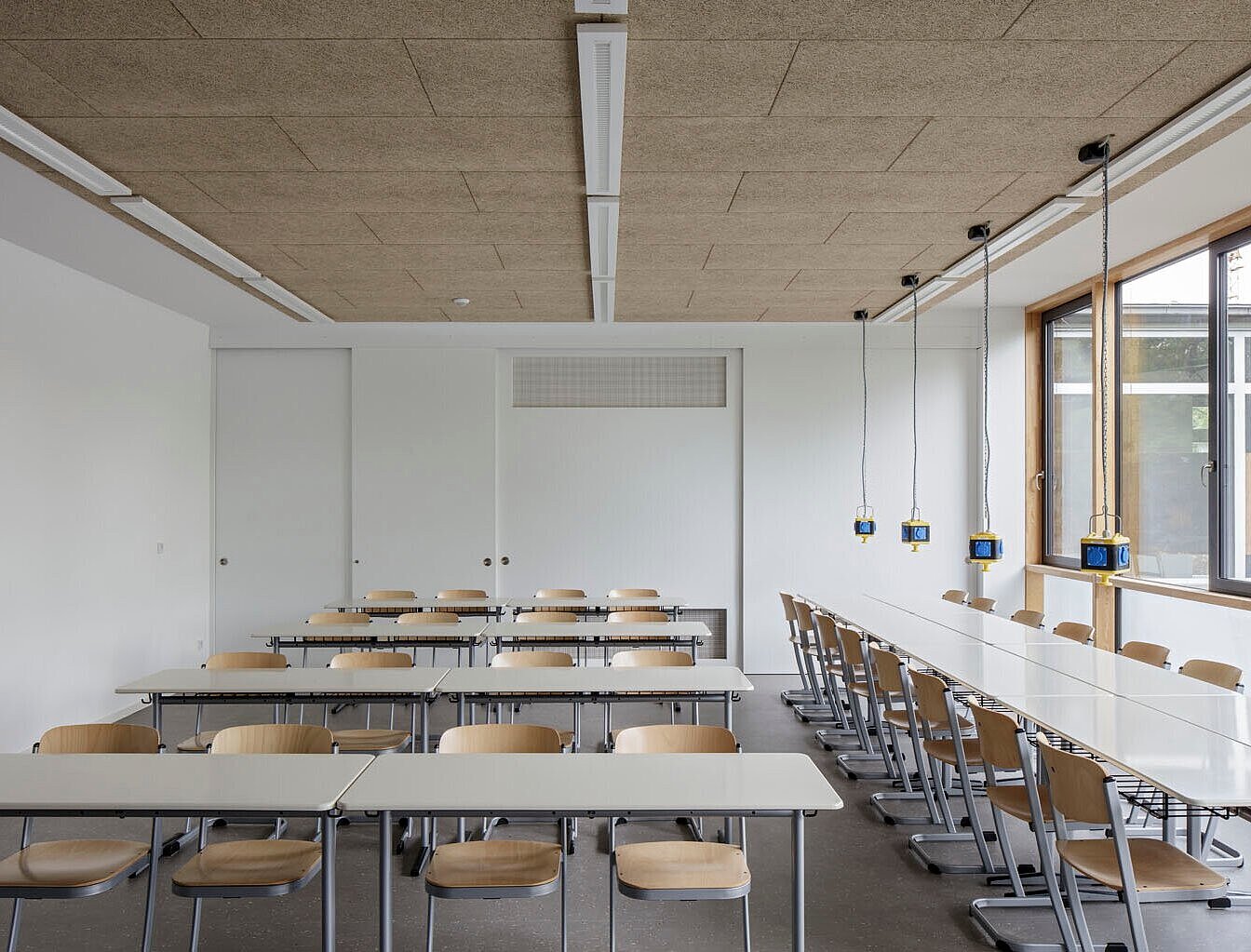 Das Bild zeigt ein saniertes Klassenzimmer mit mehreren Tischreihen und -gruppen sowie Deckensteckdosen.