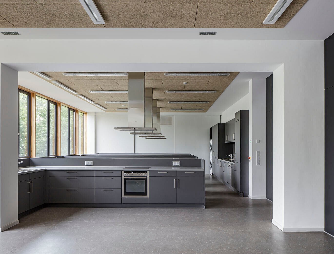 Das Bild zeigt die Schulküche mit anthrazitfarbenen Kochinseln, einschließlich Backofen und Dunstabzugshaube.