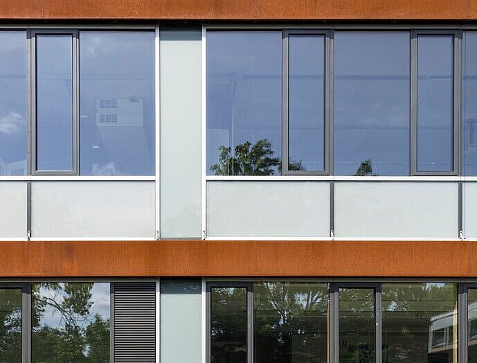 Das Bild zeigt ein Detail der Alu-Holz-Fenster mit Cortenstahl-Blenden an der Fassade.