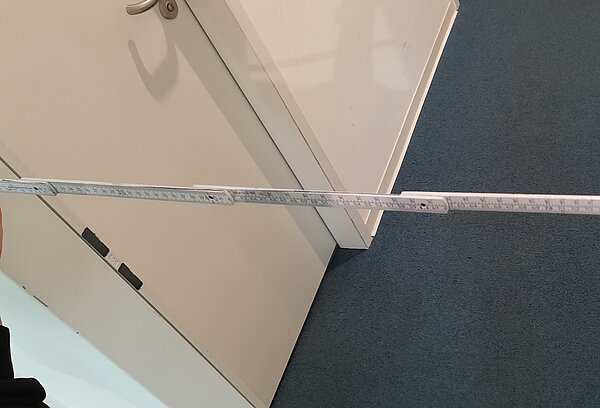 Das Bild zeigt zwei Hände, die einen Zollstock an einen Türrahmen halten.