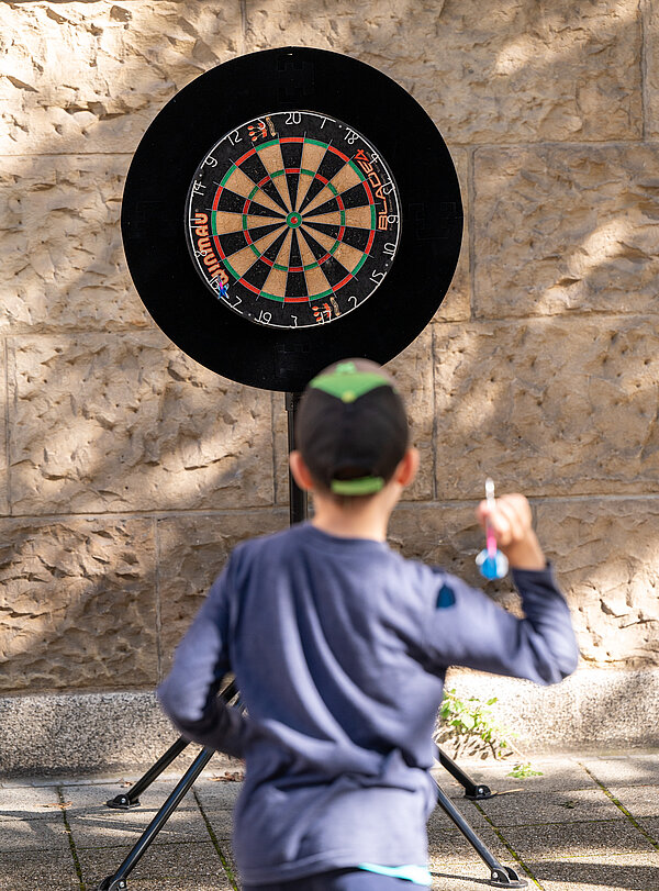 Ein Kind wirft einen Pfeil auf eine Dartscheibe.