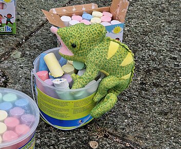 Stoffchamäleon stitzt auf Eimer mit Straßenmalkreide