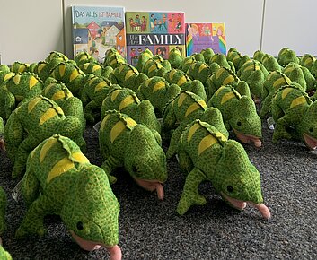 Mehere Stoffchamäleons stehen auf dem Boden vor drei Büchern