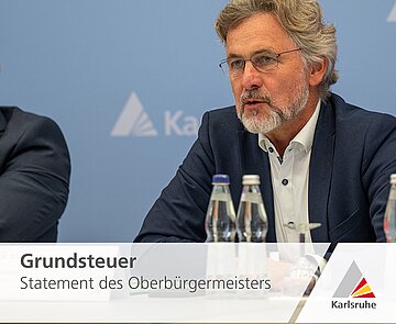 Das Bild zeigt Oberbürgermeister Dr. Mentrup vor einem blauen Hintergrund mit dem Logo der Stadt Karlsruhe.