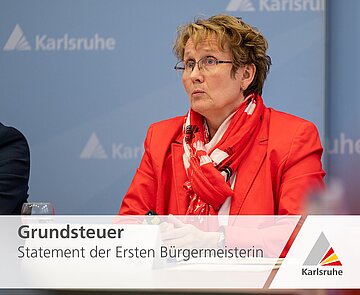 Zu sehen ist die Erste Bürgermeisterin der Stadt Karlsruhe, Frau Luczak-Schwarz, vor einem blauen Hintergrund mit dem Logo der Stadt Karlsruhe.