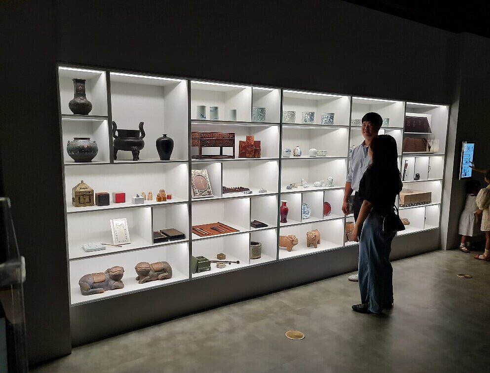 2 Personen in einem verdunktelten Raum vor einer beleuchteten Vitrine mit Ausstellungsgegenständen