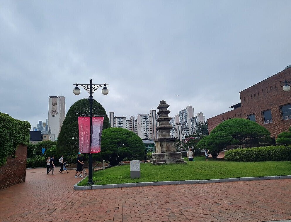 Parkähnlicher Platz mit Menschen, im Hintergrund Hochhäuser