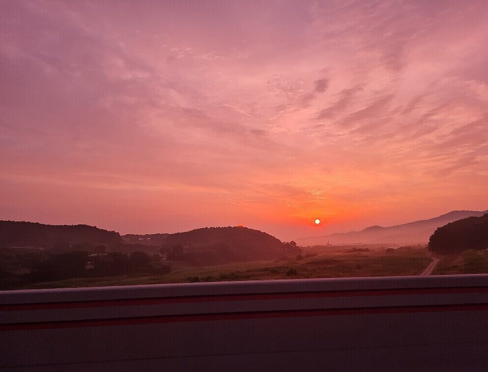 Sonnenaufgang, Himmel in rötlichem Licht, am Horizont Berge im Nebel