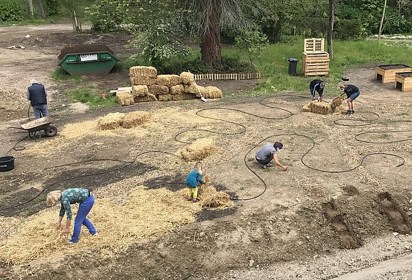 Gärtner verlegen Bewässerung und decken Boden mit Stroh ab