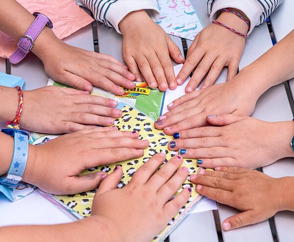 Kinder legen ihre Hände alle in die Tischmitte