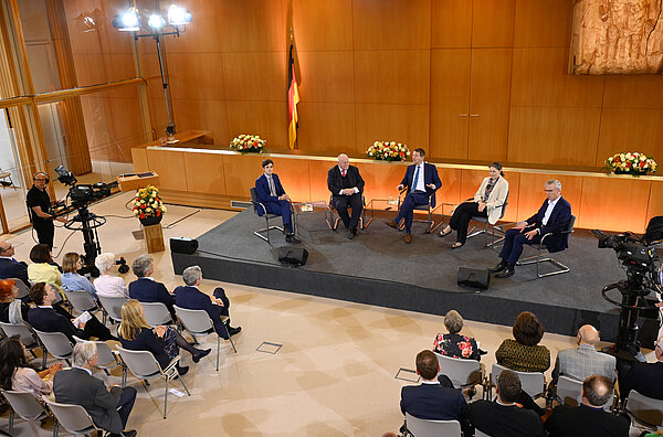 Fünf Referenten des Verfassungsgespräch 2023 sitzen vor einem Plenum und diskutieren.