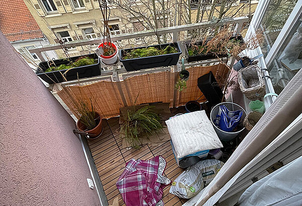 Draufsicht auf den Balkon, der voll ist mit Kübeln, Eimern, Hocker, Tuch auf dem Boden.
