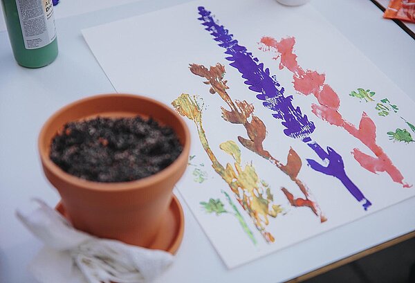 Ein Stempeldruck mit bunten Pflanzen liegt neben einem Töpfchen mit der Blumensaat.