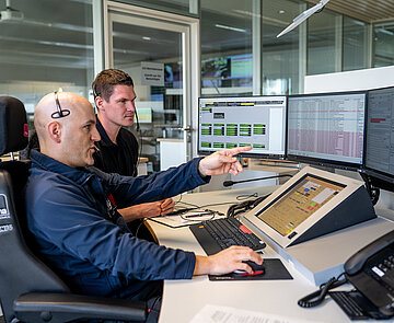 Zwei Männer betrachten einen Computerbildschirm. Einer von Ihnen zeigt dabei auf den Bildschirm