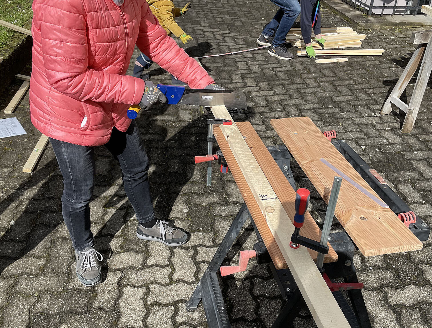 Frau die an einer klappbaren Werkbank steht und eine Latte sägt.