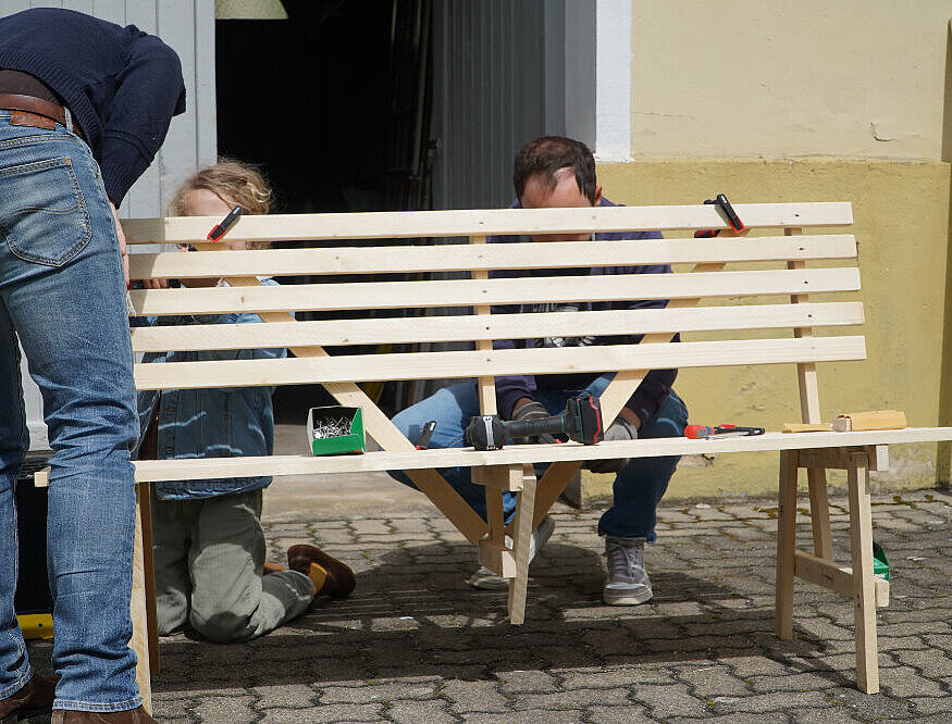 Drei Menschen, die vor und hinter einer Bank stehen und daran bauen.