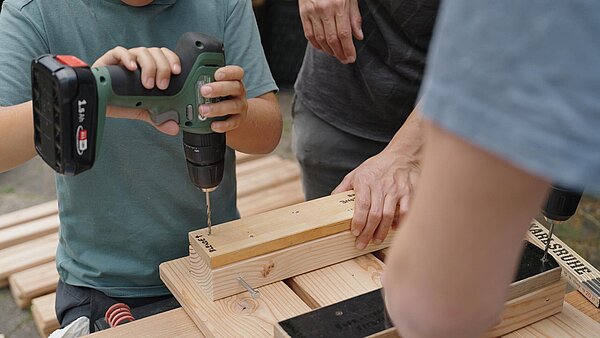 Jung mit Akkuschrauber in den Händen, schraubt in eine Holzlatte