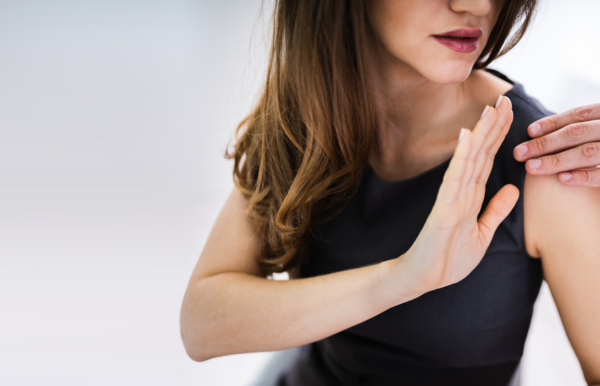 Frau wehrt mit ihrer Hand die Hand eines Mannes ab, der ihr auf die Schulter fasst. 