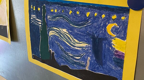 Ein farbenfrohes Kinderkunstwerk, das an einer Magnetwand in der AWO-Kita Villa ausgestellt ist, aufgenommen während der Europawochen. Das Bild zeigt eine nächtliche Szene mit Sternen und einem sichelförmigen Mond, inspiriert von Van Gogh. 