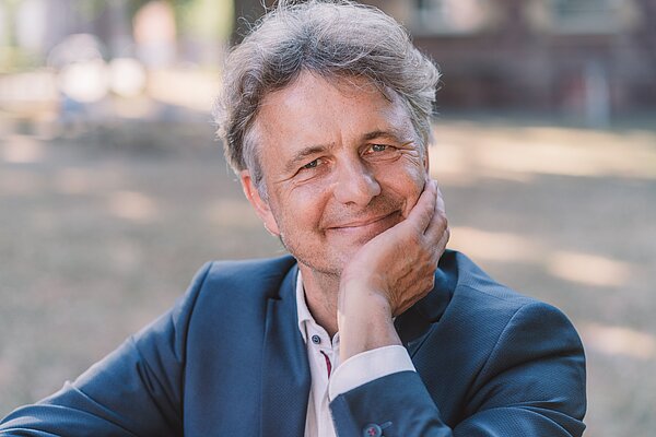 Karlsruher Oberbürgermeister Dr. Frank Mentrup stützt sein Kinn auf die Hand auf und lächelt in die Kamera.