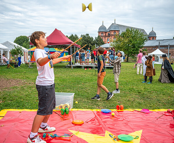 Kind spielt Diavolo, im Hintergrund das Gottesauer Schloss und andere Kinder