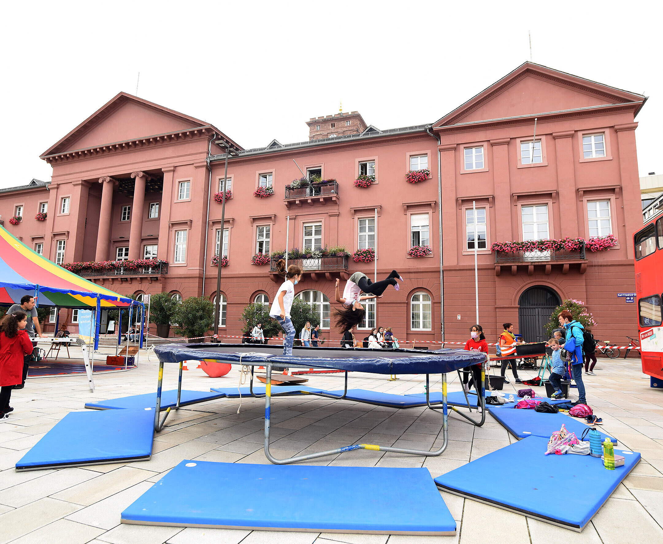 Vor dem Rathaus steht in Trampolin. Darauf springen Kinder.