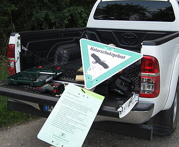 Das Bild zeigt ein weißes Dienstfahrzeug der Feldhut, mit dem eine Schutzgebietstafel transportiert wird.