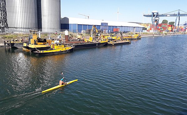 Ein Kajakfahrer  im Hafenbecken vor Industiregebäuden